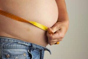 A close-up shot of a man with insulin resistance wrapping a tape measure around his stomach